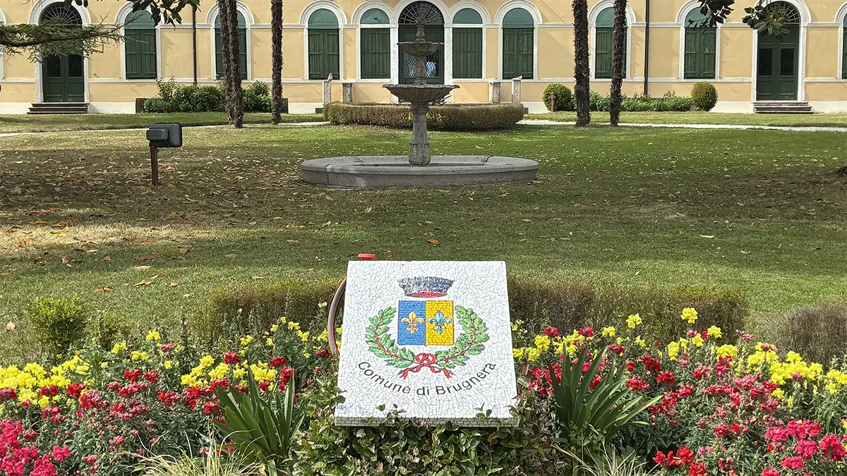 Giardino comunale di Brugnera con stemma floreale, fontana e villa sullo sfondo.