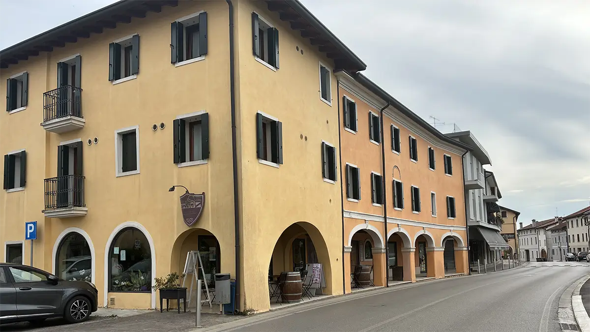 Strada di Brugnera con edifici porticati gialli e arancioni.