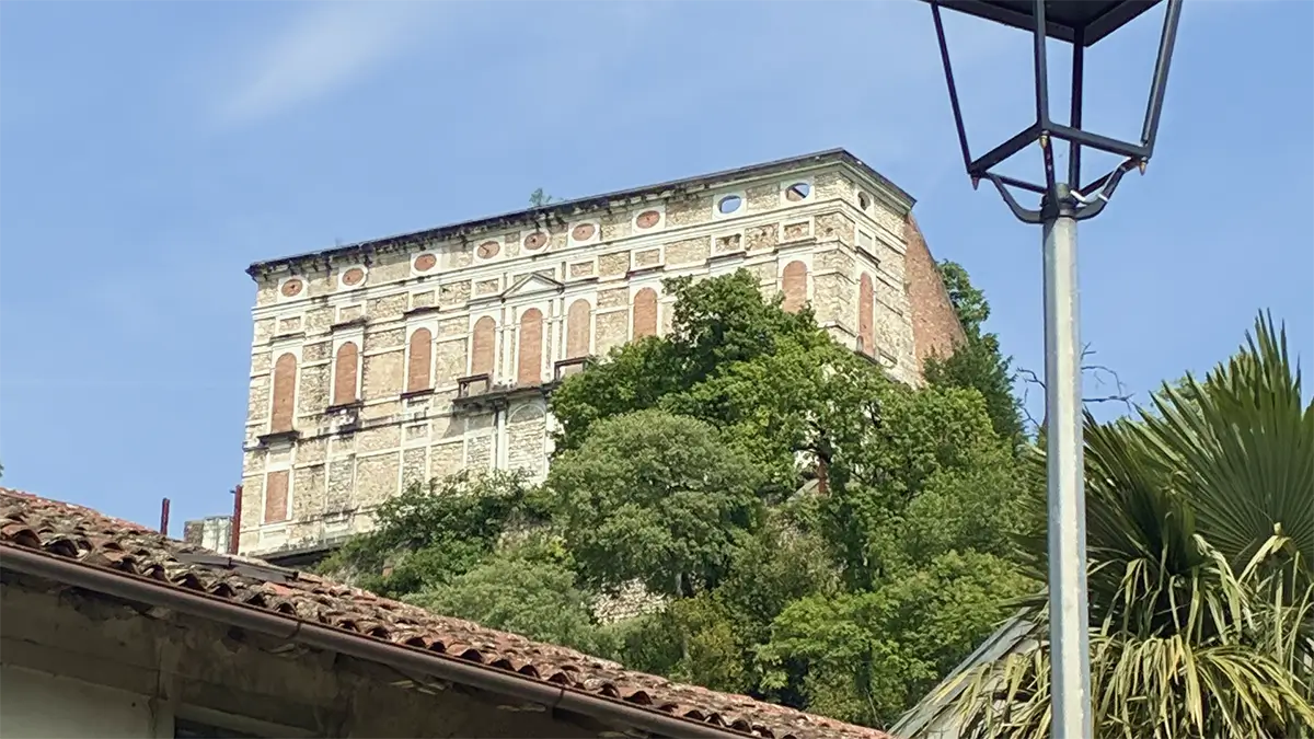 Grande edificio storico di Polcenigo visto dal basso, tra alberi e tetti in coppi.
