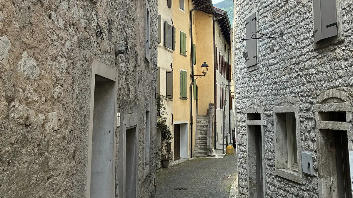Vicolo in pietra del centro storico di Polcenigo con case antiche e lampione.